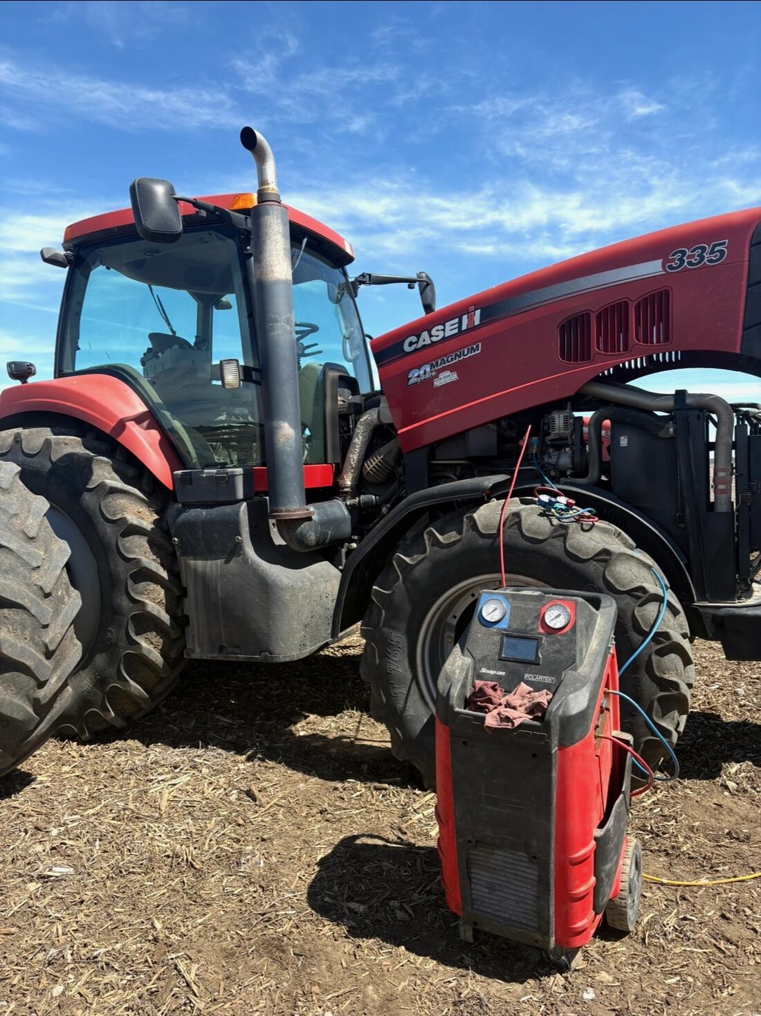 Case IH tractor with an A/C service machine beside it in a field